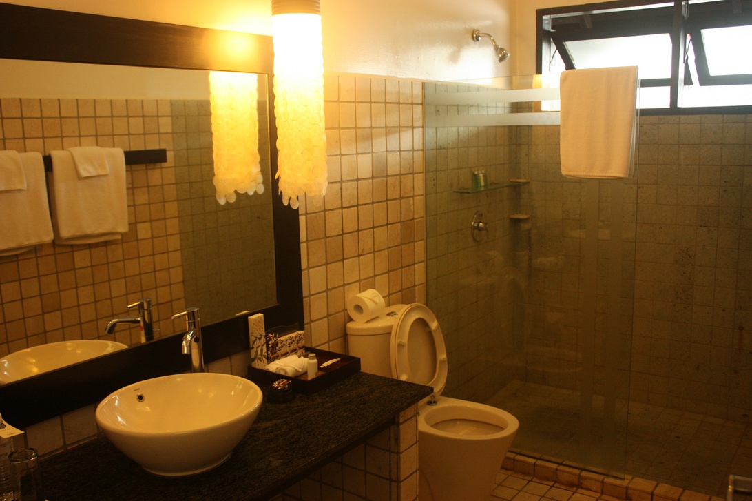 Een conventionele badkamer met beige tegels en een waskom op een donker blad.