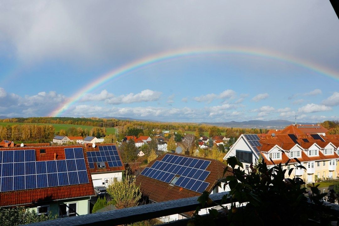 Zonnepanelen op daken van een woonwijk onder een dubbele regenboog